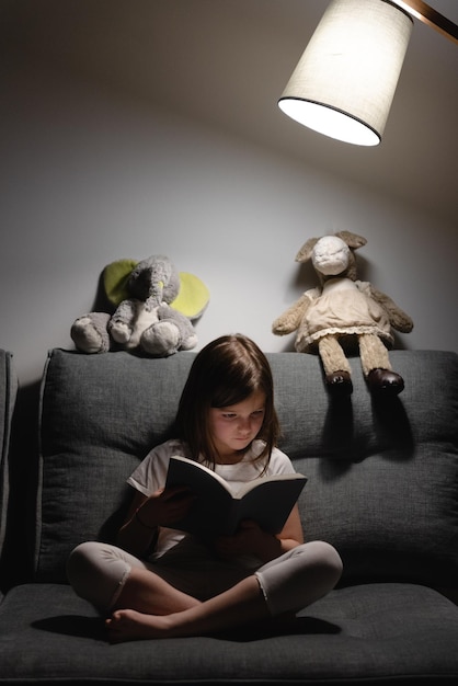 Kind, das nachts ein Buch liest, das von einer Lampe beleuchtet wird.