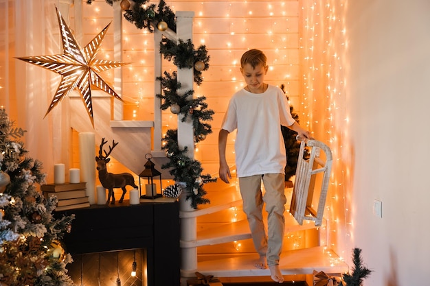 Kind, das zu Hause Weihnachtsbaum schmückt. Kleiner Junge in Strickpullover mit Weihnachtsschmuck. Familie mit Kindern feiert Winterferien. Kinder dekorieren Wohnzimmer und Kamin zu Weihnachten.