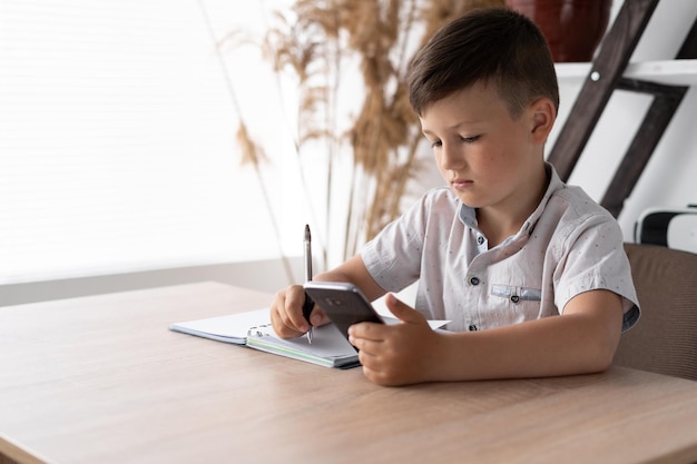 Kind der digitalen Generation, das Hausaufgaben mit einem Mobiltelefon macht Unterricht mit einem Gadget über das Internet Ein Schüler schreibt Tests von einem Smartphone Online-Bildungskonzept