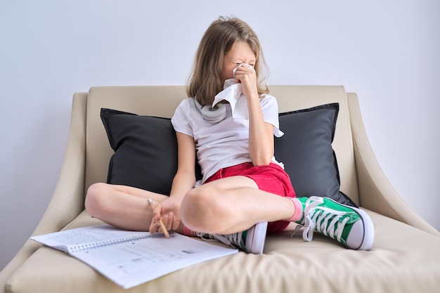 Kind der Grippesaison niest in Taschentuch Mädchen sitzt zu Hause auf der Couch und schreibt in Notizbuch