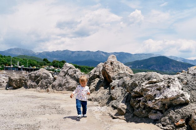 Kind geht auf einer Steinplattform mit Felsbrocken vor dem Hintergrund der Berge
