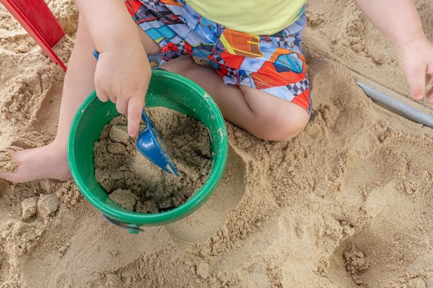 Kind gräbt an sonnigen Tagen ein Loch in sauberen Strandsand, während die Familie mit Schaufel und Plastikeimer spielt und Spaß hat