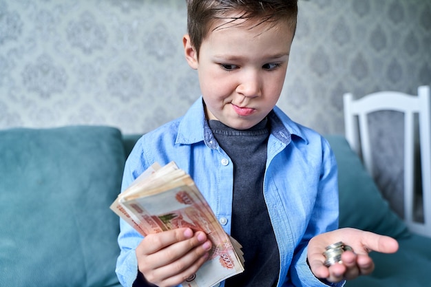 Kind hat viel Geld in der einen Hand und kleine Münzen in der anderen und Zweifel