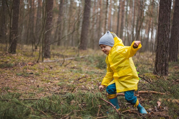 Kind im gelben Regenmantel spaziert nach Regen und Spaß im Wald