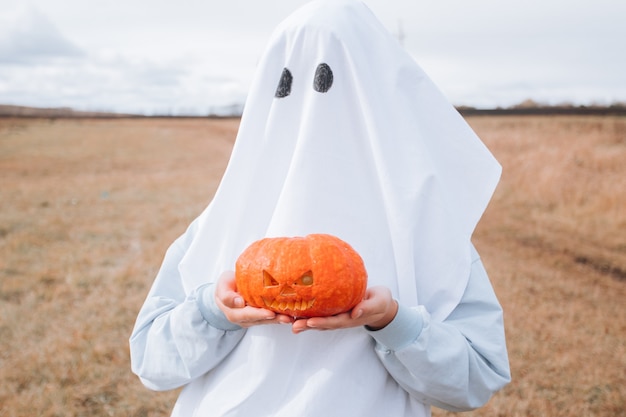 Kind im Halloween-Kostüm, das geschnitzten Kürbis hält. Halloween Süßes oder Saures