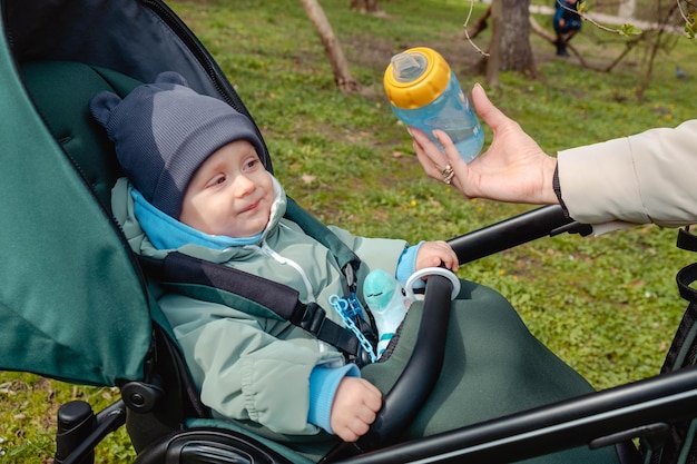 Kind im Kinderwagen, der die Flasche im Frühlingspark betrachtet