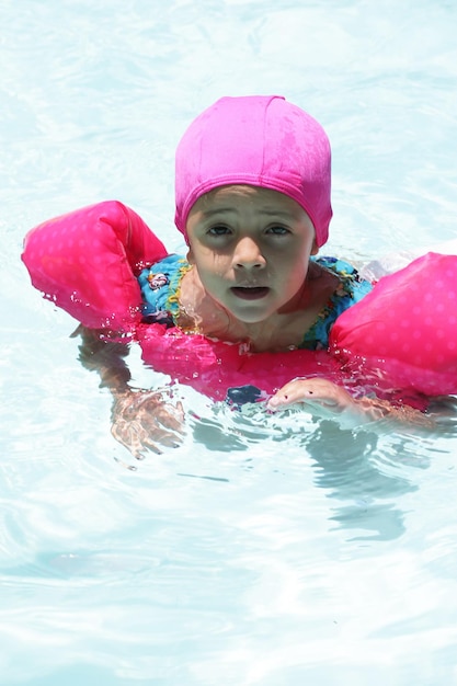 Kind im Poolschwimmen mit rosa Schwimmer mit blauem Wasser