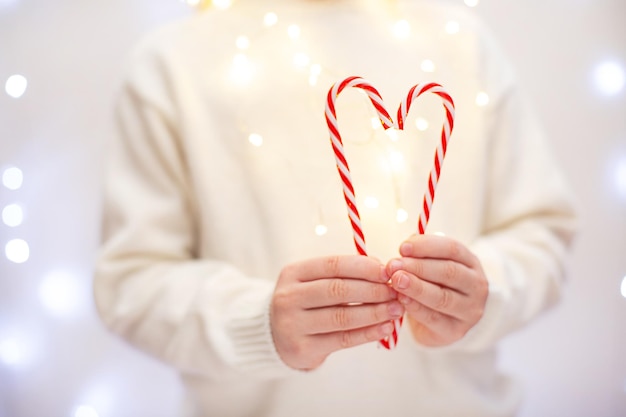 Kind im weißen Pullover hält einen herzförmigen Lutscherstock auf hellem Bokeh-Hintergrund