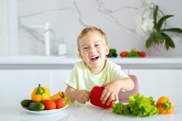 Kind in der Küche zu Hause, das Gemüse isst Baby lächelt gesundes Ernährungskonzept Vegetarier