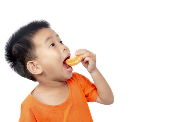 Kind in der orange Ausstattung essen die Orange, die auf weißem Hintergrund lokalisiert wird