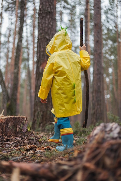Kind in einem gelben Regenmantel, der im Wald spazieren geht, und lustige Rückansicht