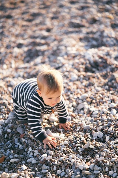 Kind in einem gestreiften Overall krabbelt über einen Kiesstrand