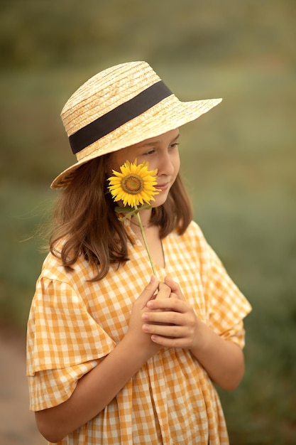 Kind in einem karierten Kleid hält eine Sonnenblume in den Händen und lächelt