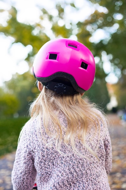 Foto kind in einem rosa helm von hinten im park