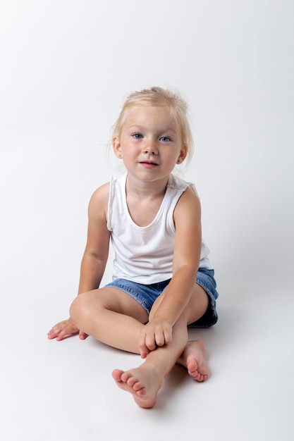 Kind in einem T-Shirt, Shorts, die im Studio auf hellem Hintergrund sitzen.