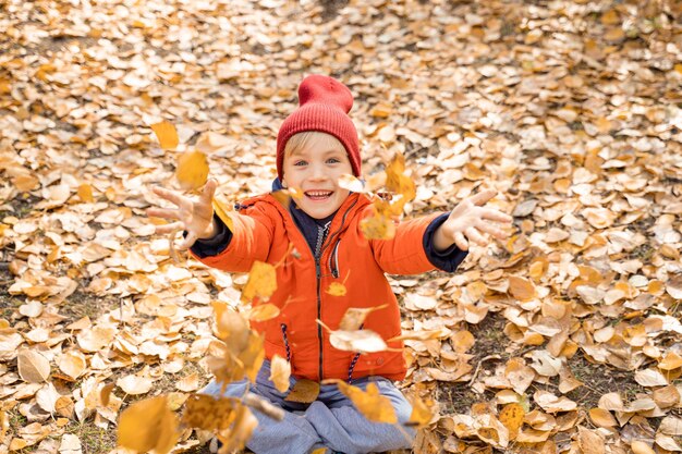 Kind in einer orangefarbenen Jacke sitzt auf den gefallenen Blättern im Herbstwald Ruhen Sie sich im Herbst in der Natur aus