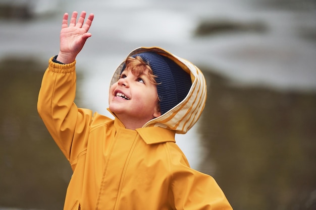 Kind in gelbem wasserdichtem Mantel und Stiefeln, die nach dem Regen im Freien spielen