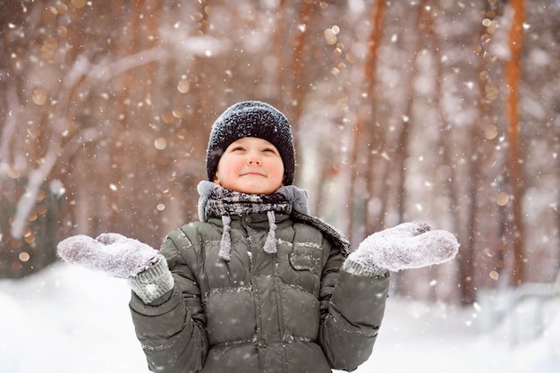 Kind in Handschuhen streckt ihre Hand, um fallende Schneeflocken zu fangen.