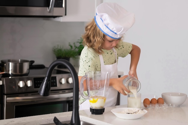 Kind in Kochmütze und Schürze, die Zubereitung von Speisen in der Küche Kochen von Kindern Kind Junge mit Schürze und Kochmütze, die eine gesunde Mahlzeit in der Küche zubereiten Kochprozess