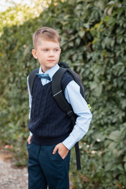 Kind in Schuluniform mit Rucksack geht vor dem Hintergrund einer Kletterpflanze zur Schule