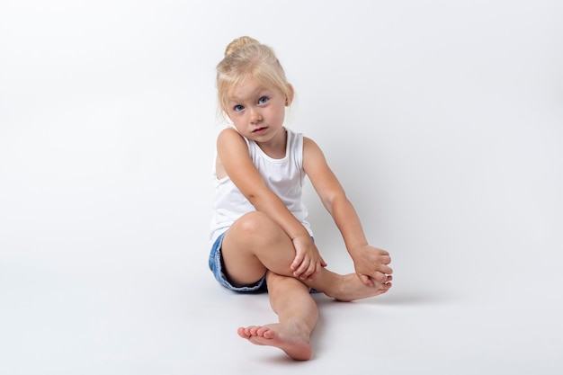 Kind in T-Shirt-Shorts sitzt im Studio auf hellem Hintergrund