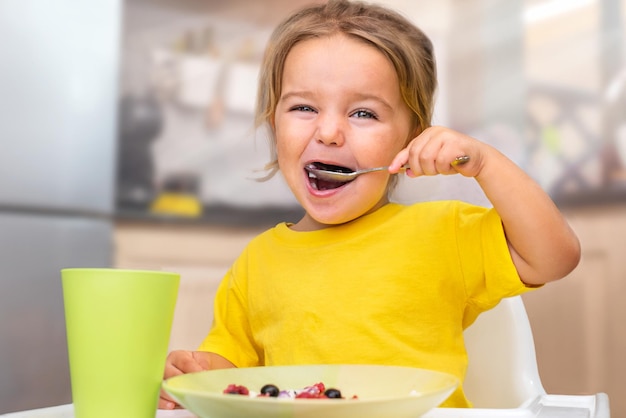 Kind isst Brei mit Beeren in einem Hochstuhl in der Küche