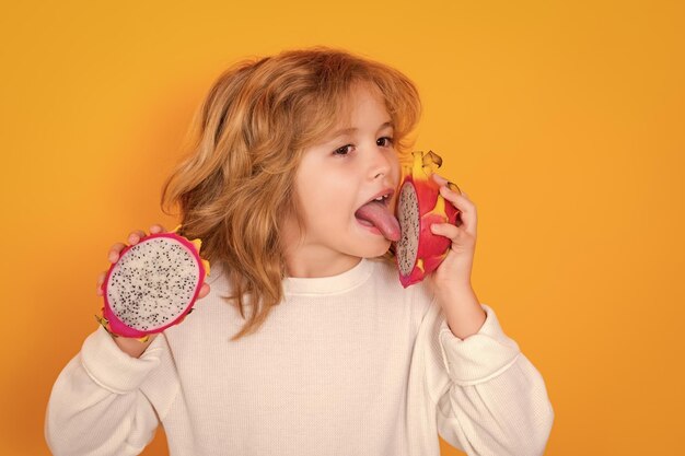 Foto kind isst drachenfrucht im studio studio-porträt von süßem kind mit drachenfrüchte isoliert auf gelbem hintergrund