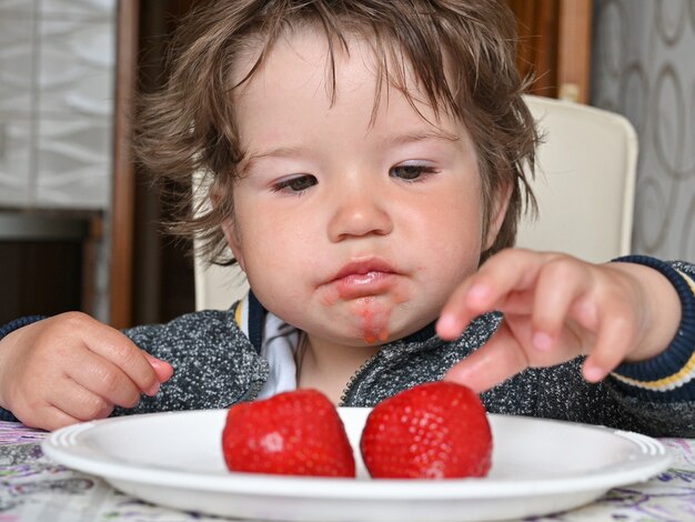 Kind isst reife rote Erdbeeren von einem weißen Teller. Nahaufnahme