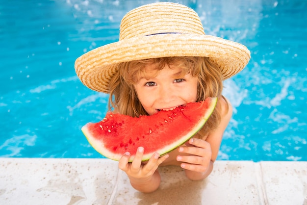 Kind isst Wassermelone im Pool süßer Junge isst Scheibe rote Wassermelone am Strand glücklicher Kaukasier...