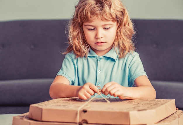 Kind ist erstaunt über eine große Kiste mit einem riesigen Pizzen sehr überrascht und glücklich Kleiner Junge hält Pizzakartons Junge bereit, eine Pizza zu essen Kleines Kind, das einen Pizzakarton betrachtet