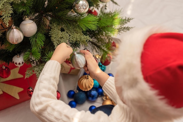 Kind Junge in roter Weihnachtsmütze schmückt Weihnachtsbaum Nahaufnahme Weihnachten oder Neujahr gemütliches Urlaubskonzept Selektiver Fokus