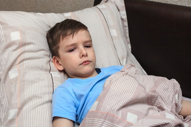 Kind Junge liegt mit missfallenem Gesicht auf dem Bett, ist krank. Quarantäne zu Hause.