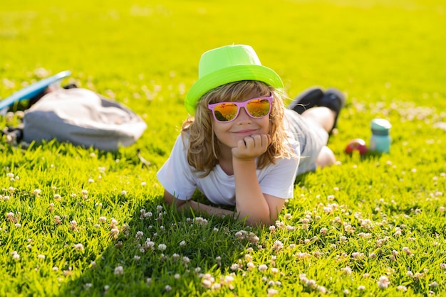 Kind, Junge, Mädchen, das auf grünem Gras ruht, glückliches Kind, das auf der Wiese genießt und Sommerferien träumt