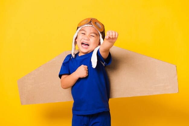 Kind kleiner Junge Lächeln tragen Pilot Hut spielen und Schutzbrille mit Spielzeug Pappe Flugzeug Flügel