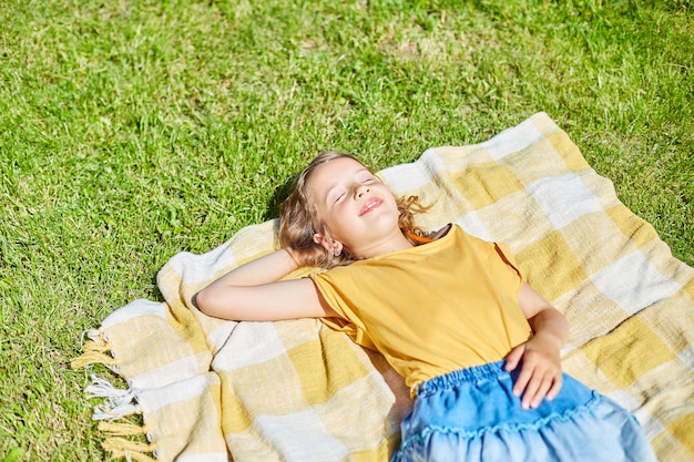 Kind liegt auf der Decke, auf dem Gras am Sonnentag, kleines Mädchen nimmt ein Sonnenbad im Hinterhofhaus