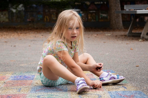 Kind Mädchen blondes Vorschulalter wird auf dem Bürgersteig sitzend gespielt