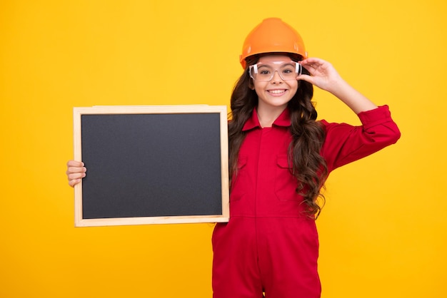 Kind Mädchen Builder in Hard Hat Helm Teenager-Mädchen Arbeiter halten Tafel isoliert auf gelbem Hintergrund Kinder Renovierungskonzept Copy Space Mock-up