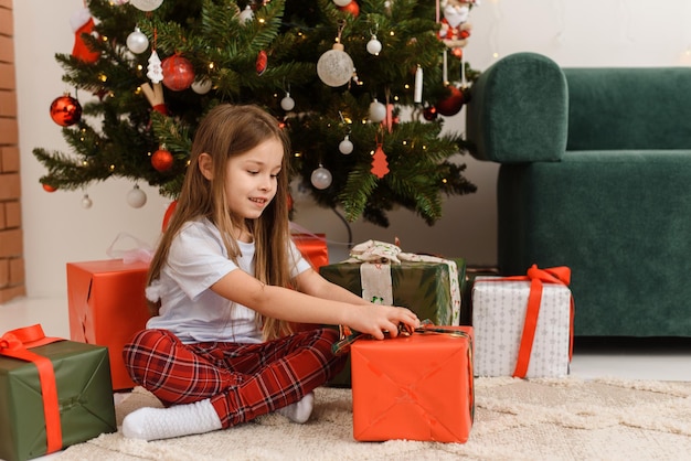 Kind Mädchen im Schlafanzug öffnet ein Geschenk am Weihnachtsmorgen Frohes neues Jahr