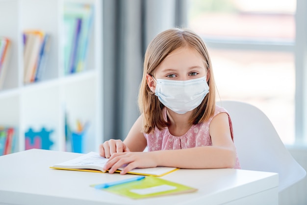 Kind Mädchen in der medizinischen Maske, die an der Schule studiert