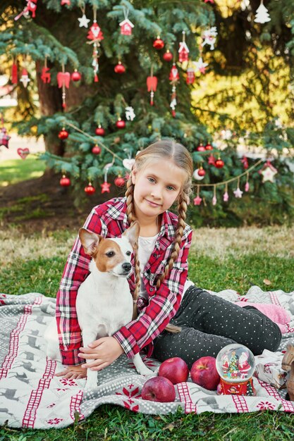 Kind Mädchen mit Hund Jack Russell Terrier in der Nähe des Weihnachtsbaumes mit Geschenken,