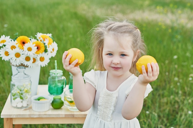 Kind Mädchen mit Limonade. Limonade und Gänseblümchenblumen auf Tisch.