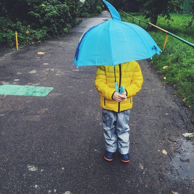 Kind mit blauem Regenschirm steht auf der Straße