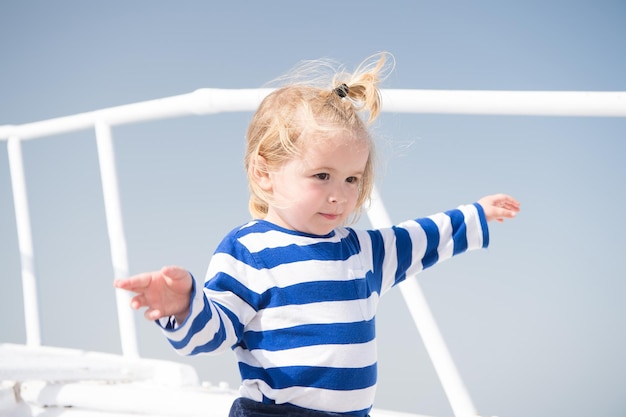 Kind mit blonden Haaren auf der Yacht an einem sonnigen Tag. Junge im Matrosenhemd am blauen Himmel. Abenteuer, Entdeckung, Fernweh. Reiseziel, Kreuzfahrt, Reisen. Sommerferienkonzept.