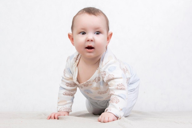 Kind mit einem Lächeln auf weißem Hintergrund Ein entzückendes sechs Monate altes Baby krabbelt auf dem Bett