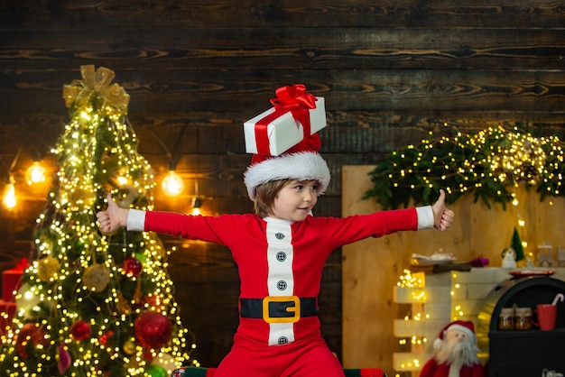 Kind mit einem Weihnachtsgeschenk auf Holzhaushintergrundgeschenkgefühlen nach Hause Weihnachtsatmosphäre