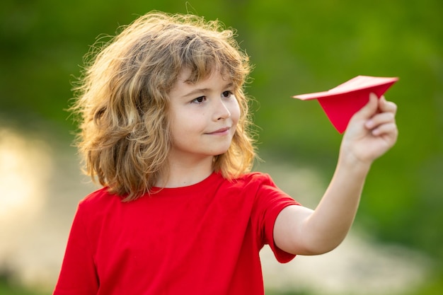 Kind mit Flugzeug, süßes blondes Kind, träumt, fliegen, spielen, Papierflieger, Wachstum im Freien, Kinderkonzept, glückliches Kind