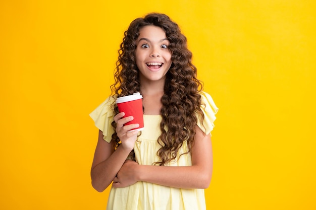 Kind mit Kaffee- oder Teetasse isoliert auf gelbem Studiohintergrund Teenager-Mädchen nehmen Getränk mit