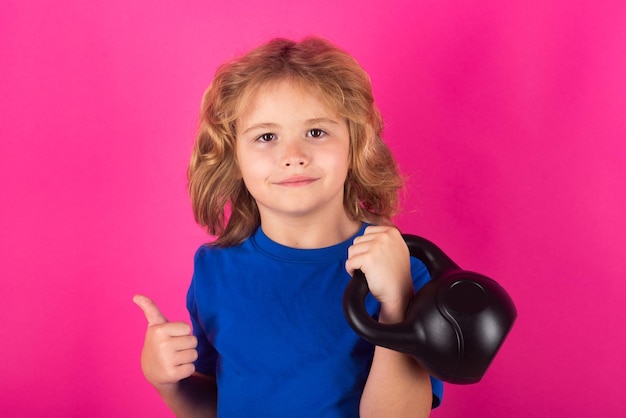 Kind mit Kettlebell im Studio auf rotem rosa Hintergrund Netter kleiner Junge, der Übungen mit Kettlebell macht Porträt des sportlichen Kindes mit Hanteln Glückliches Kind, Junge, der trainiert