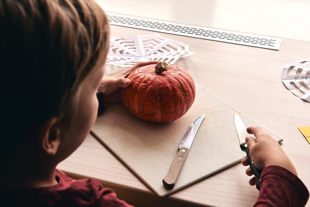 Kind mit Messer, das Kürbis oder Kürbislaterne schnitzt. Mama verbringt Zeit mit Sohn zusammen.