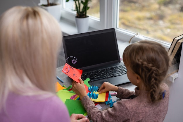 Kind mit Mutter hat Spaß beim Ausschneiden von Scherenpapier im Vorschulalter. Mutter und Tochter machen Papierhandwerk